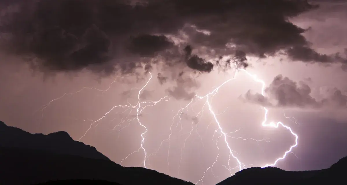 Gewitter in den Bergen: Blitze zucken durch dunkle Wolken über silhouettierten Gipfeln. Ein dramatisches Naturschauspiel.