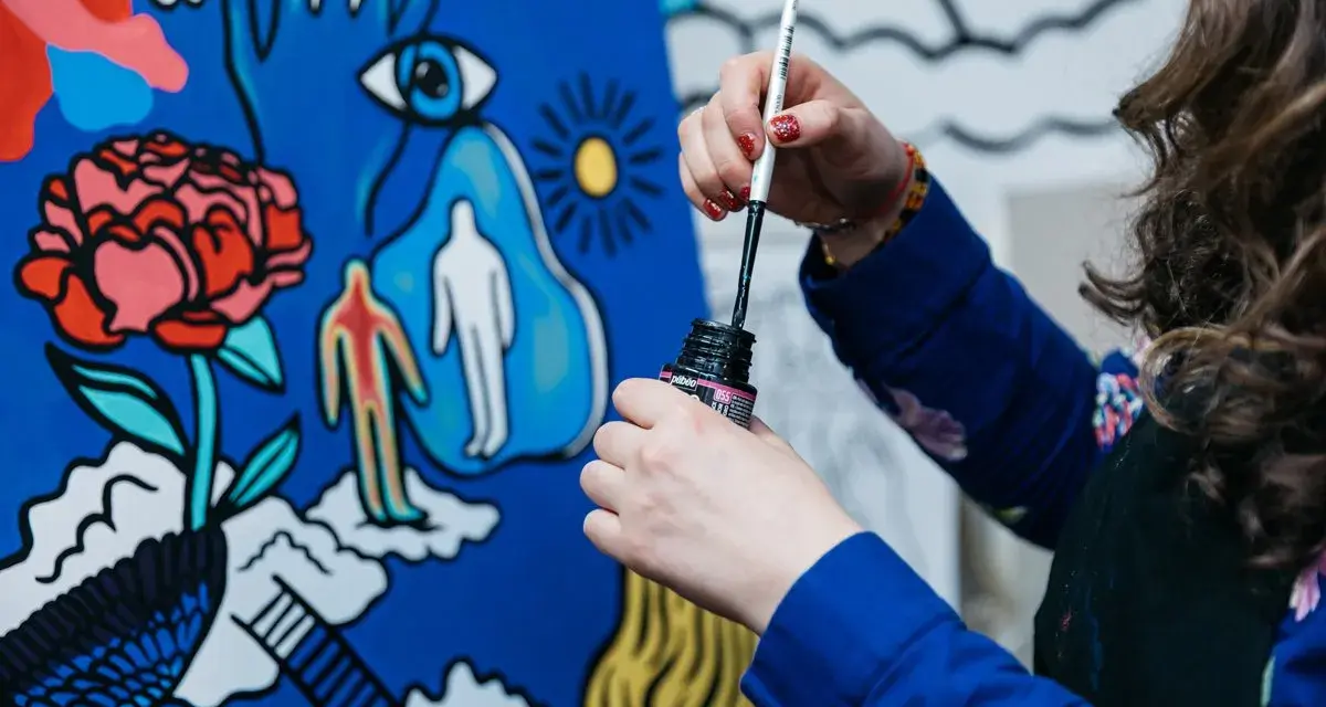 Une artiste, dans son métier artistique, trempe son pinceau dans l'encre pour peindre une toile aux motifs surréalistes : une fleur, un œil, des silhouettes.