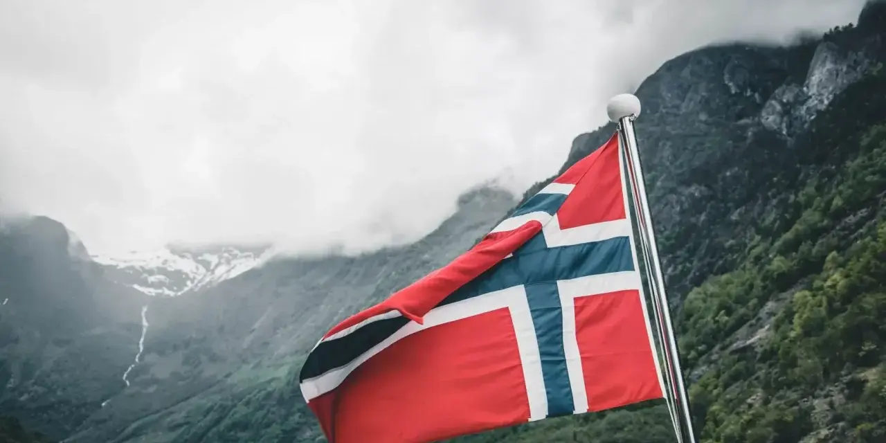 Norweska flaga na tle fiordu. Marzenie o wysokich zarobkach w Norwegii staje się rzeczywistością.
