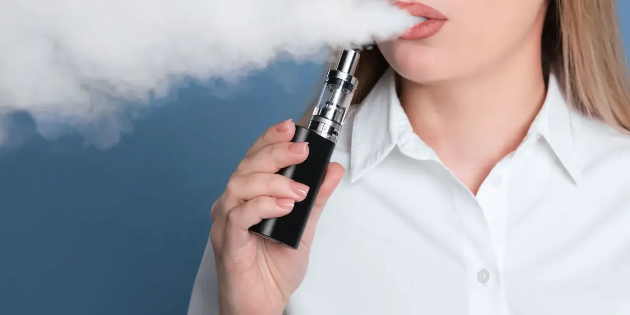 Mujer exhala vapor de un vaper, una alternativa moderna al tabaco tradicional.