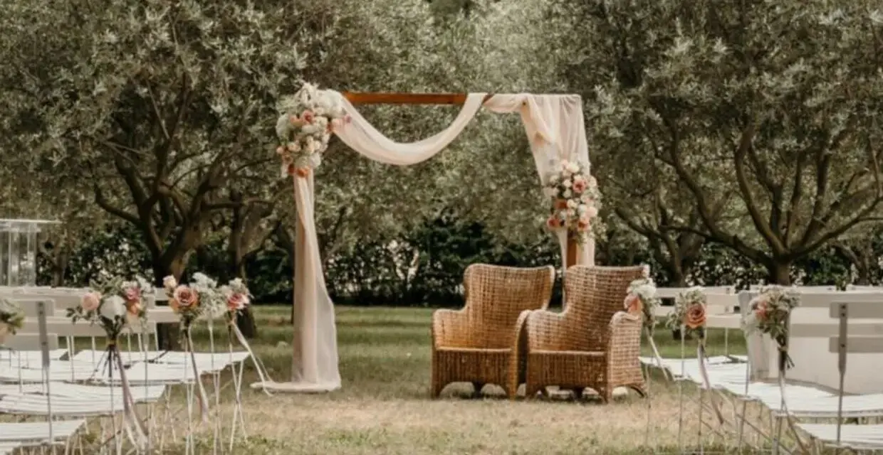 Un décor champêtre pour une célébration laïque : chaises blanches, arche fleurie, fauteuils en rotin sous les oliviers.