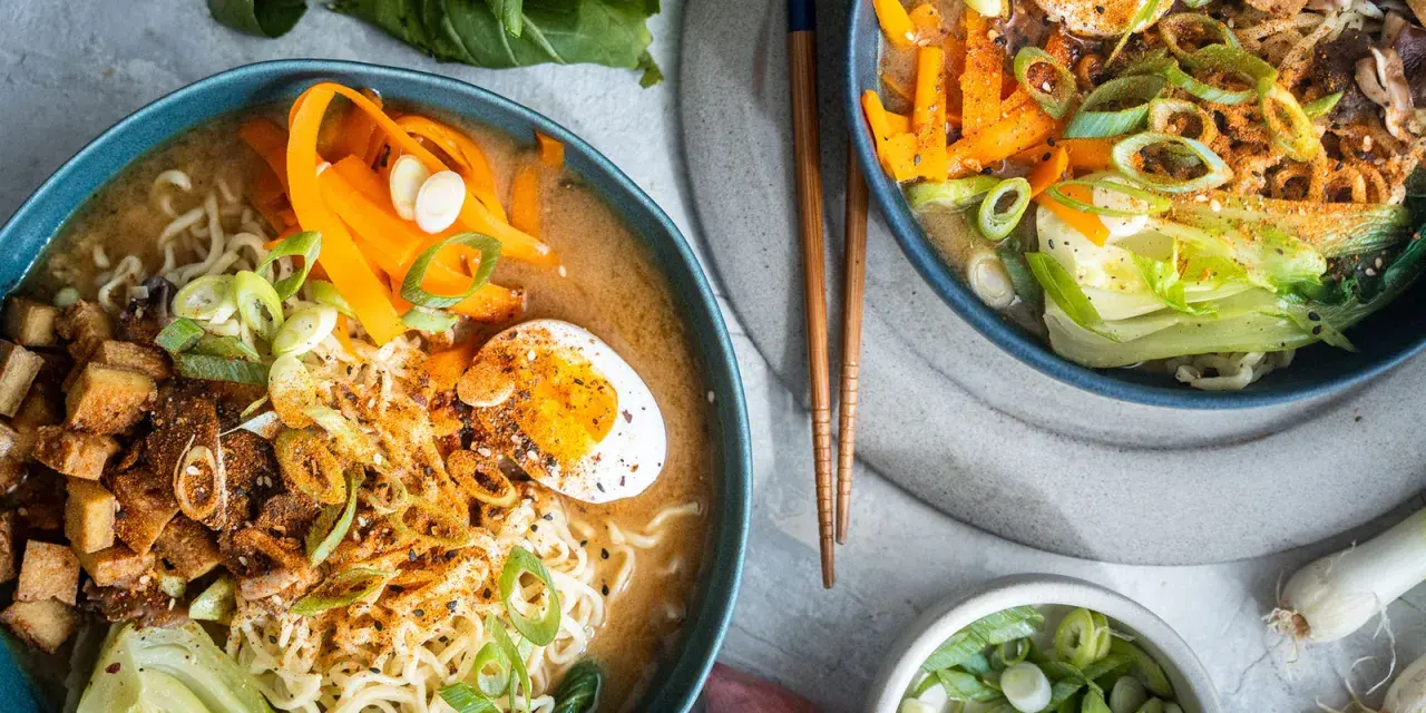 Zwei Schüsseln dampfendes Miso Ramen mit Nudeln, Ei, Karotten, Pak Choi und Frühlingszwiebeln.