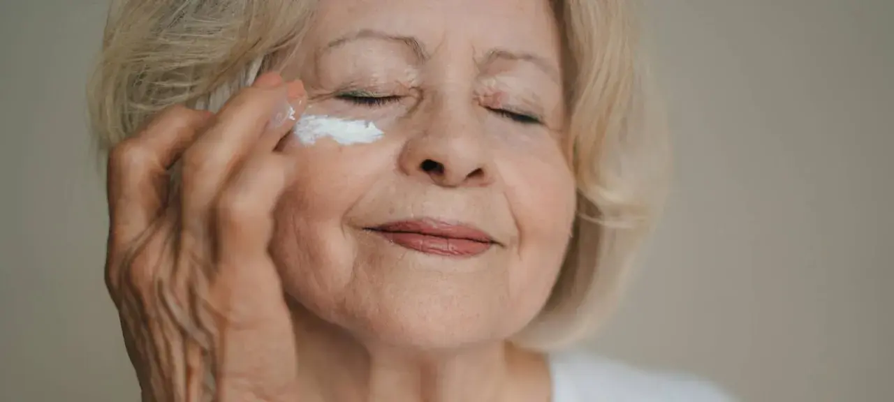 Eine Frau über 70 trägt eine feuchtigkeitsspendende Creme auf. Ihre Augen sind geschlossen, während sie sich um ihre Haut kümmert.
