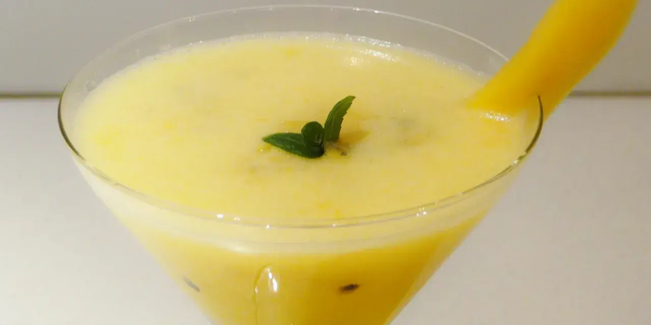 Orzeźwiający drink z marakują, ozdobiony listkiem mięty i kawałkiem mango.