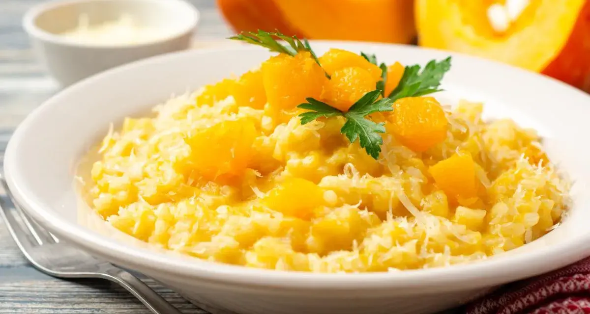 Un cremoso risotto de calabaza, adornado con trozos de calabaza y perejil fresco, espolvoreado con queso rallado.