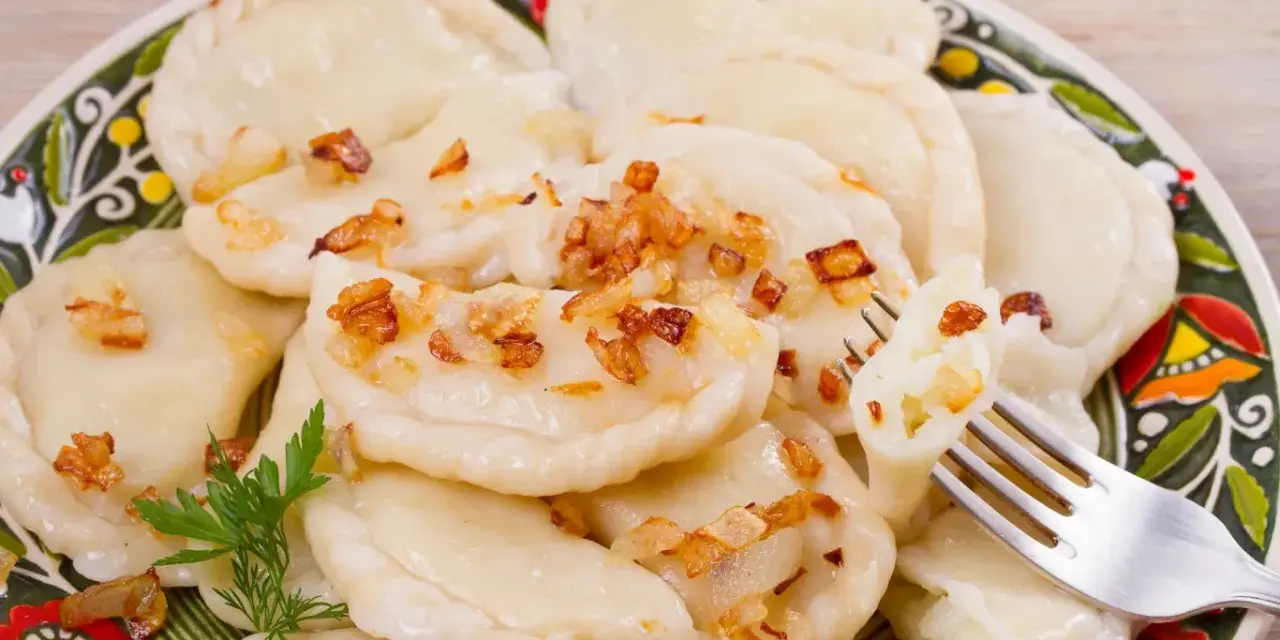 Pyszne pierogi ruskie z farszem Magdy Gessler, posypane skwarkami. Na talerzu z tradycyjnym wzorem.
