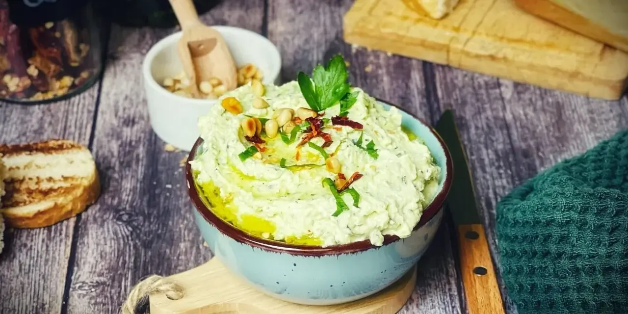Cremiger Zucchini-Dip mit Pinienkernen und Kräutern, serviert mit geröstetem Brot.