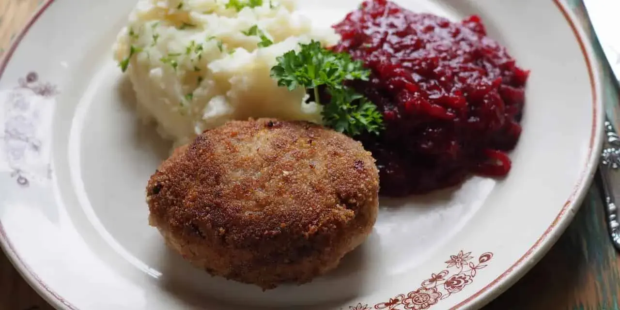 Kotlet mielony z ziemniakami i żurawiną, udekorowany natką pietruszki.