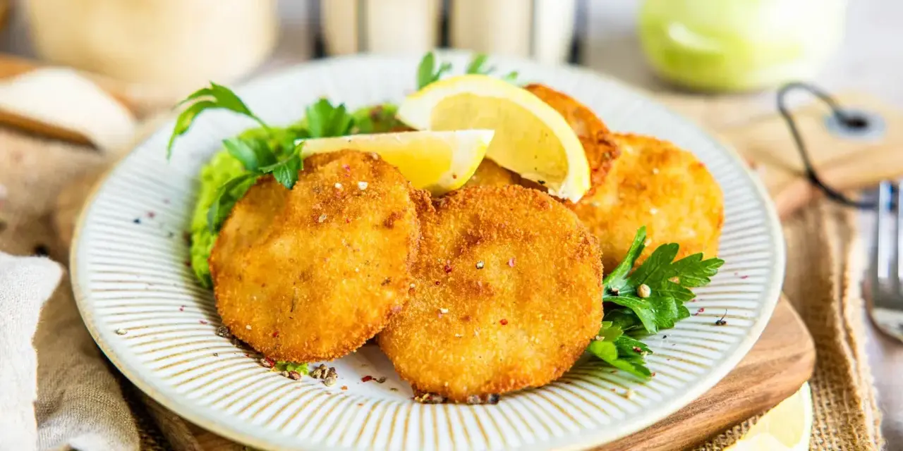 Knusprige Kohlrabi-Schnitzel auf einem Teller mit Erbsenpüree, Zitrone und Petersilie. Ein köstliches vegetarisches Gericht.