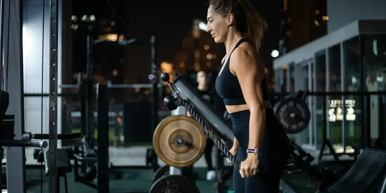 Kobieta ćwiczy na siłowni, korzystając z wyciągu. Jej karta multisport pozwala na takie wieczorne treningi.