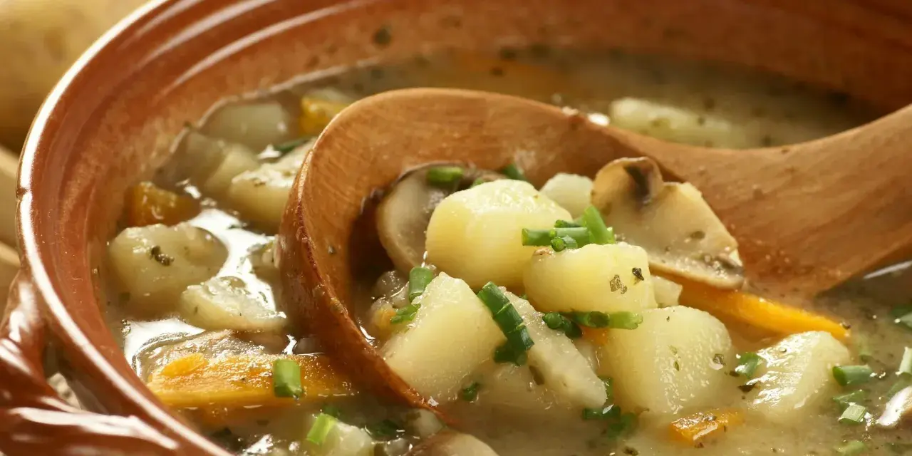 Gęsta zupa ziemniaczana z grzybami i marchewką, jak z przepisu babci. Drewniana łyżka zanurzona w aromatycznym bulionie.