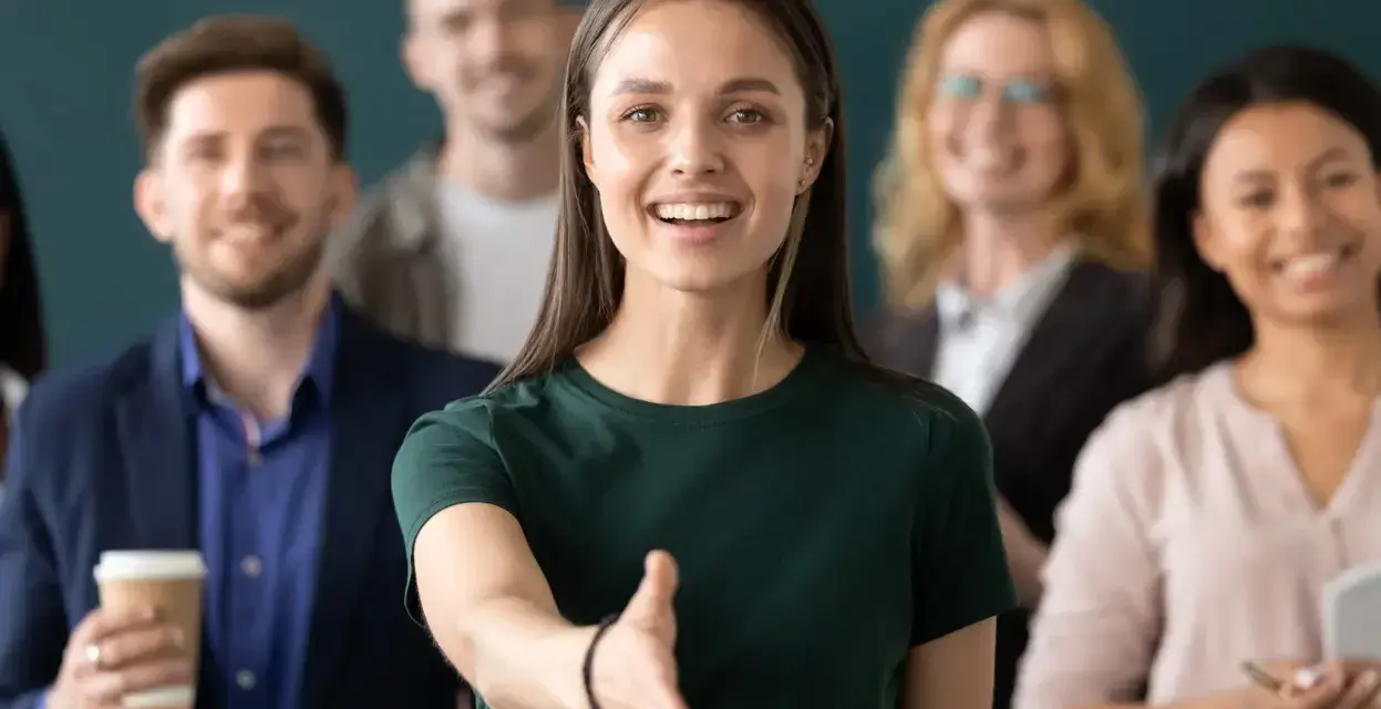 Uśmiechnięta kobieta wyciąga rękę na powitanie. To jej pierwszy dzień w nowej pracy, a zespół wygląda na przyjazny.