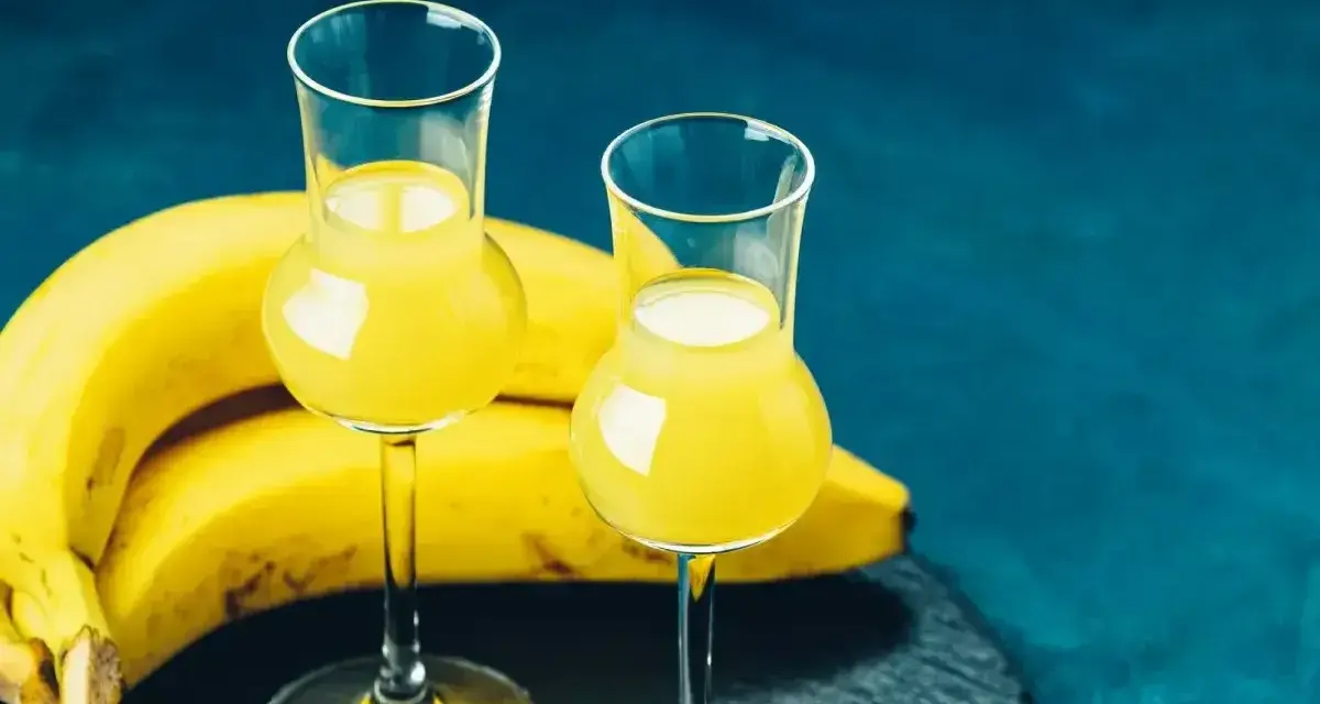 Dwa kieliszki z żółtym likierem bananowym obok dojrzałych bananów. Idealny przepis na domowy likier bananowy.