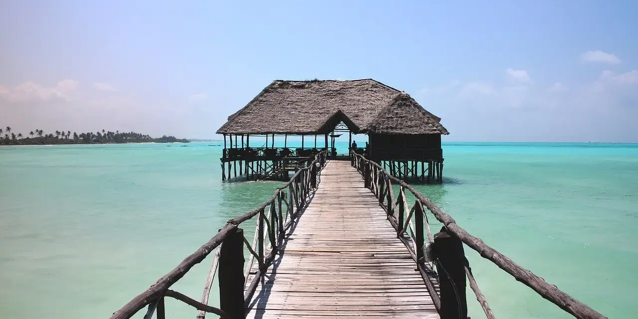 Drewniany pomost prowadzi do chatki na palach na turkusowej wodzie. Idealne miejsce na wiza zanzibar.