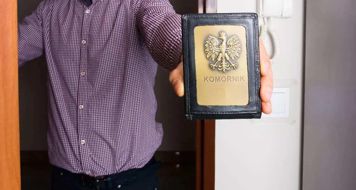 Mężczyzna w kratę pokazuje legitymację komornika. Zastanawiasz się, ile może zabrać komornik?