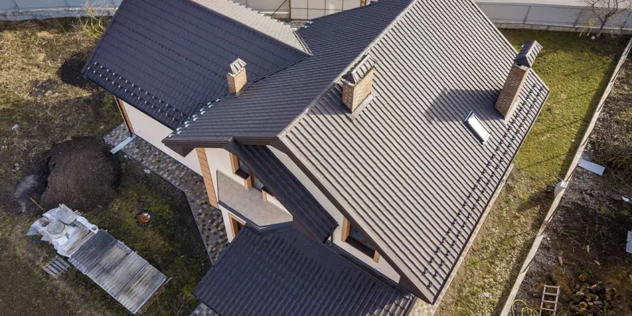 Dachówka na dachu domu, z widocznym kominem, który przypomina rzygownik.