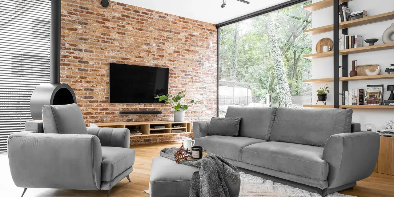 Nowoczesne, szare komplety wypoczynkowe z funkcją spania Black Red White. Wygodna sofa i fotel przy ceglanej ścianie.
