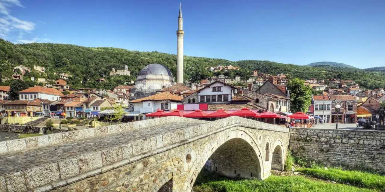 Kamienny most nad rzeką, z widokiem na meczet i miasto na wzgórzu. Kosowo atrakcje turystyczne zachwycają.
