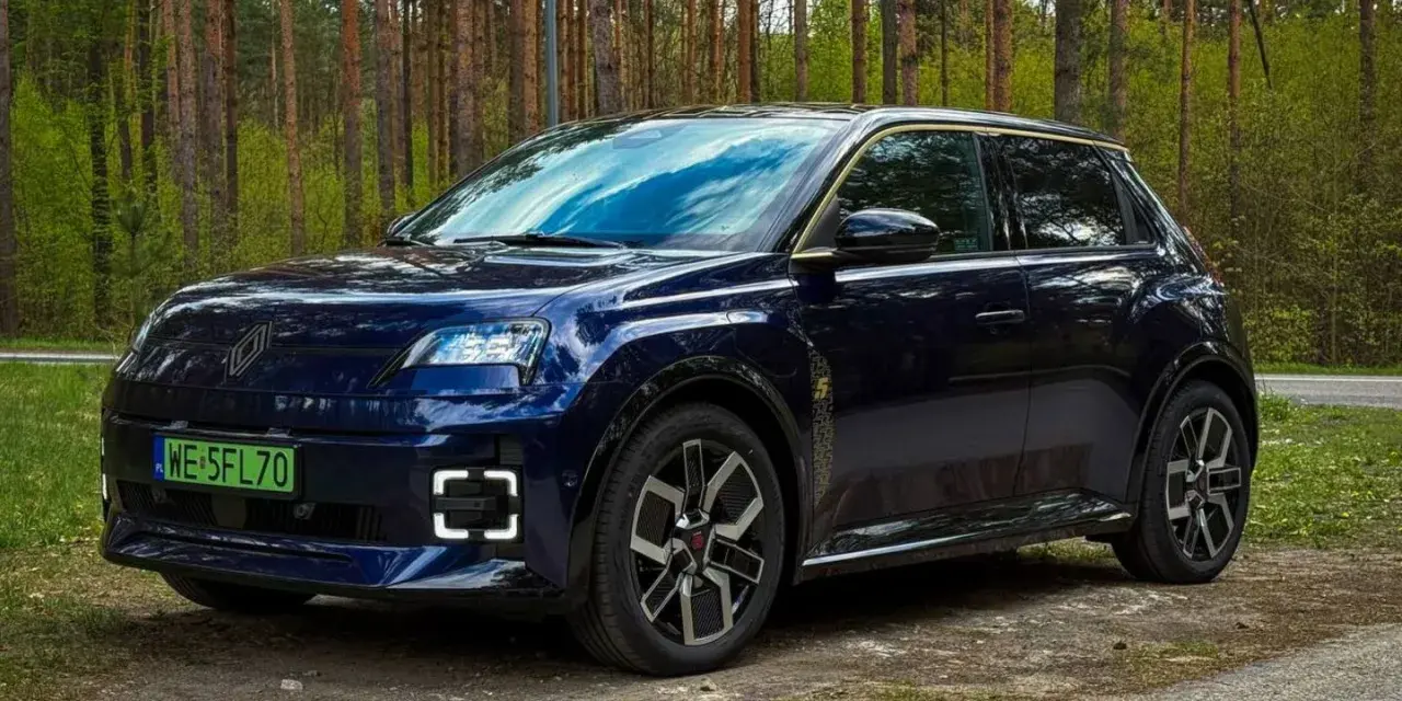 Ciemnoniebieski Renault 5 E-Tech elektryczny stoi na drodze leśnej.