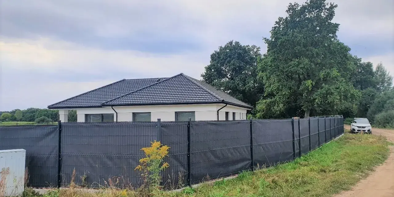 Ciemnoszara siatka na ogrodzeniu panelowym, idealna jako czym zasłonić ogrodzenie panelowe. Dom i samochód w tle.