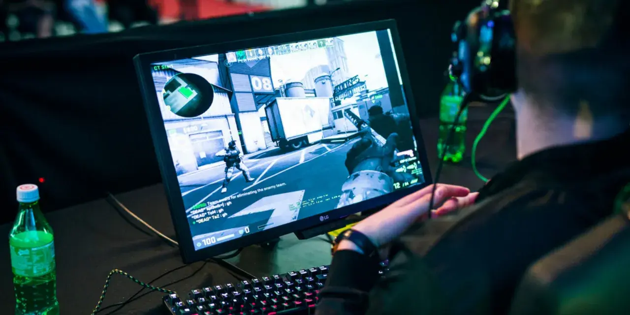 Gracz w słuchawkach gra w CS:GO, próbując jak zmniejszyć ping. Na ekranie widać akcję z gry i klawiaturę.