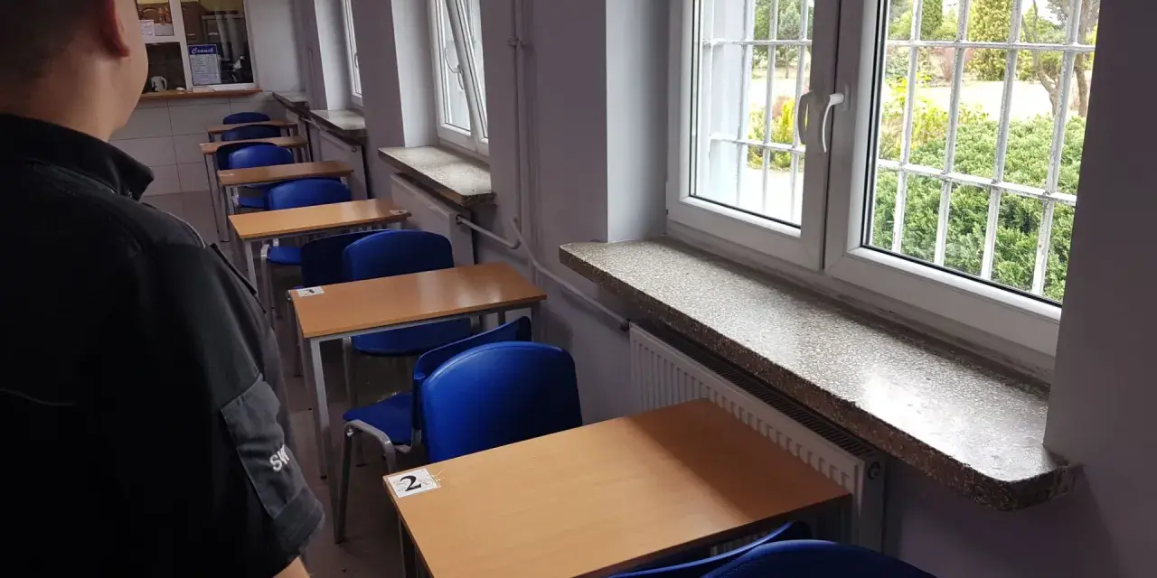 Rzędy pustych ławek i krzeseł w sali lekcyjnej. Za kratami okien widać zieleń. To może być sala egzaminacyjna w więzieniu na Białołęce.