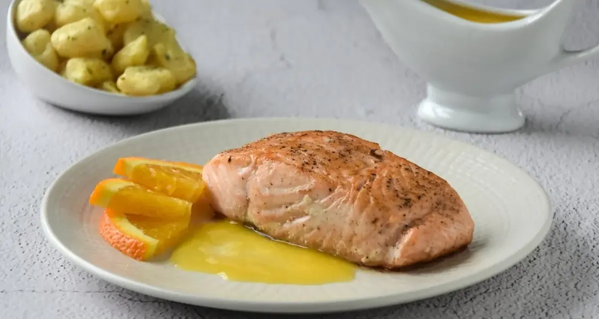 Filete de salmón a la naranja, servido con gajos de naranja y una salsa dorada. Acompañado de patatas pequeñas.
