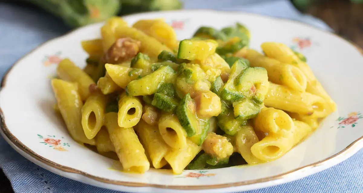 Piatto di pasta penne con zucchine a rondelle e cubetti di pancetta croccante, condita con una salsa cremosa.