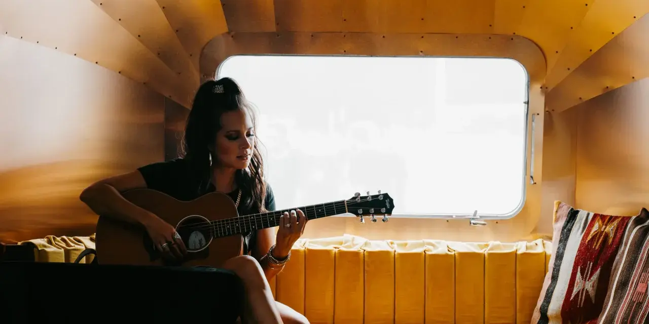 Sarah Jones, piosenkarka, gra na gitarze w przytulnym wnętrzu.