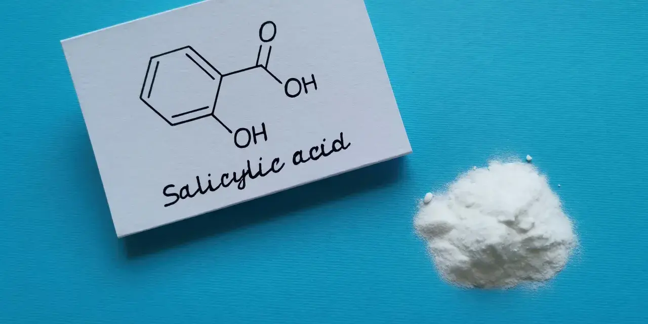 Karta z wzorem chemicznym kwasu salicylowego i jego proszkiem. Dowiedz się, jak stosować kwas salicylowy.