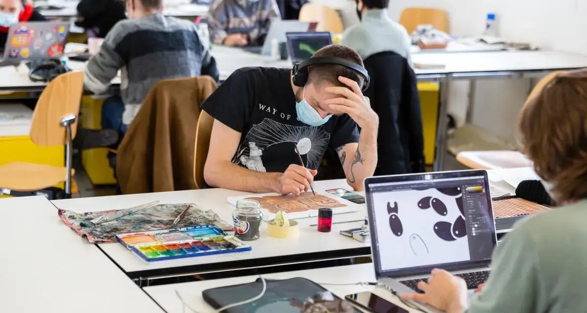 Des étudiants concentrés dans une école d'art, certains peignent, d'autres travaillent sur ordinateur. L'ambiance est studieuse.