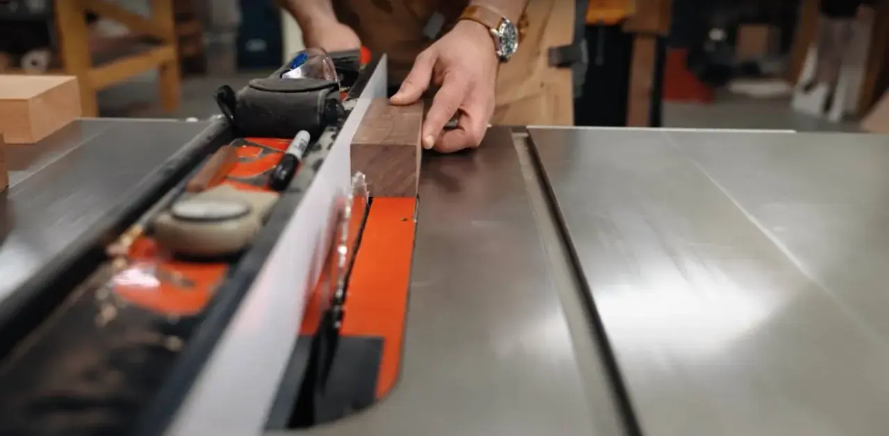 Hands guide a wooden plank along a table saw's fence, demonstrating how to use a table saw for precise cuts.