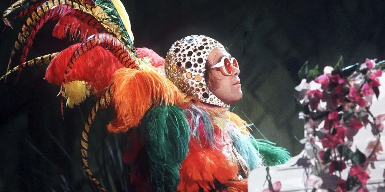 Elton John in einem extravaganten Federkostüm, das an einen Pfau erinnert. Seine ikonischen Elton John Outfits sind legendär.