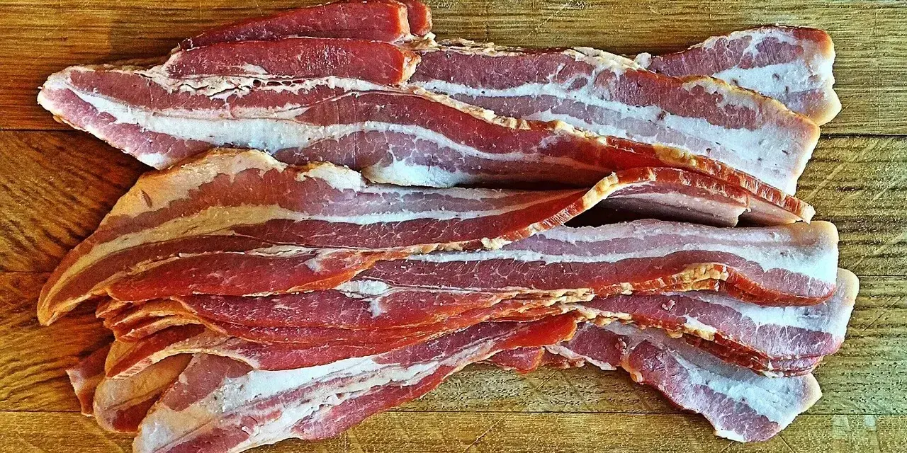Surowy boczek ułożony na drewnianej desce. Idealny do chrupiącego smażenia, ale pamiętaj o jego kaloryczności - boczek kcal.