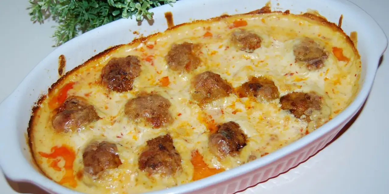 Pulpety w sosie śmietanowo-serowym, zapieczone w naczyniu, z zieloną dekoracją w tle.