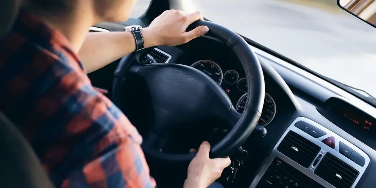 Mężczyzna w kratę prowadzi samochód, wiedząc jak jeździć po wymianie oleju. Na desce rozdzielczej widać zegary i radio.