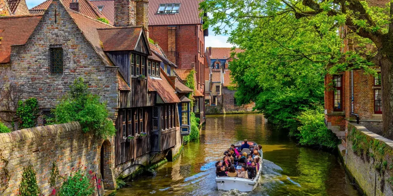 Giro in barca sui canali di Bruges, un'ottima idea per cosa vedere a Bruges in un giorno, tra case storiche e vegetazione lussureggiante.
