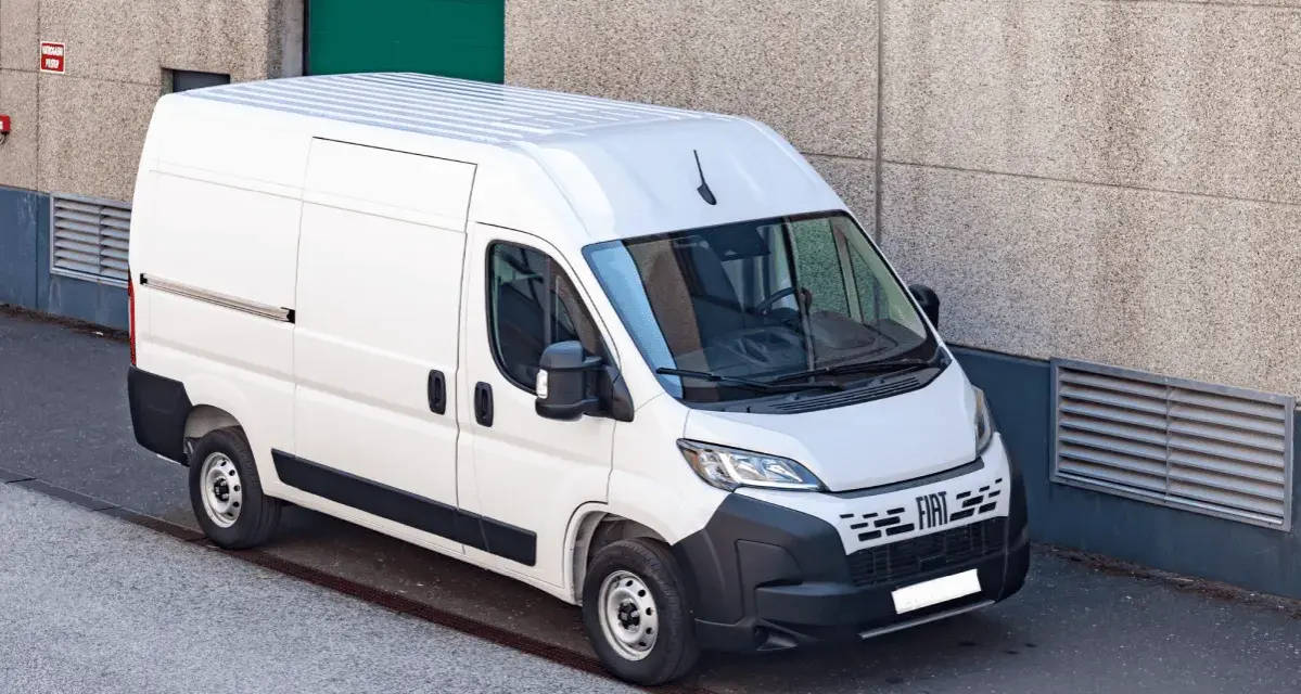 Biały bus dostawczy Fiat Ducato zaparkowany przy betonowej ścianie budynku.