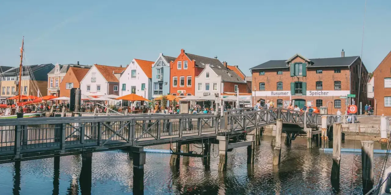 Bunte Häuser am Hafen, ein Steg führt über das Wasser. Perfekt für Ausflüge in Husum, mit Cafés und dem alten Speicher.
