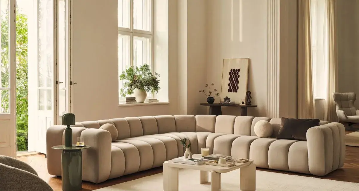 Ampio divano componibile color crema, dalle forme morbide e arrotondate, perfetto per definire le dimensioni di un salotto moderno.