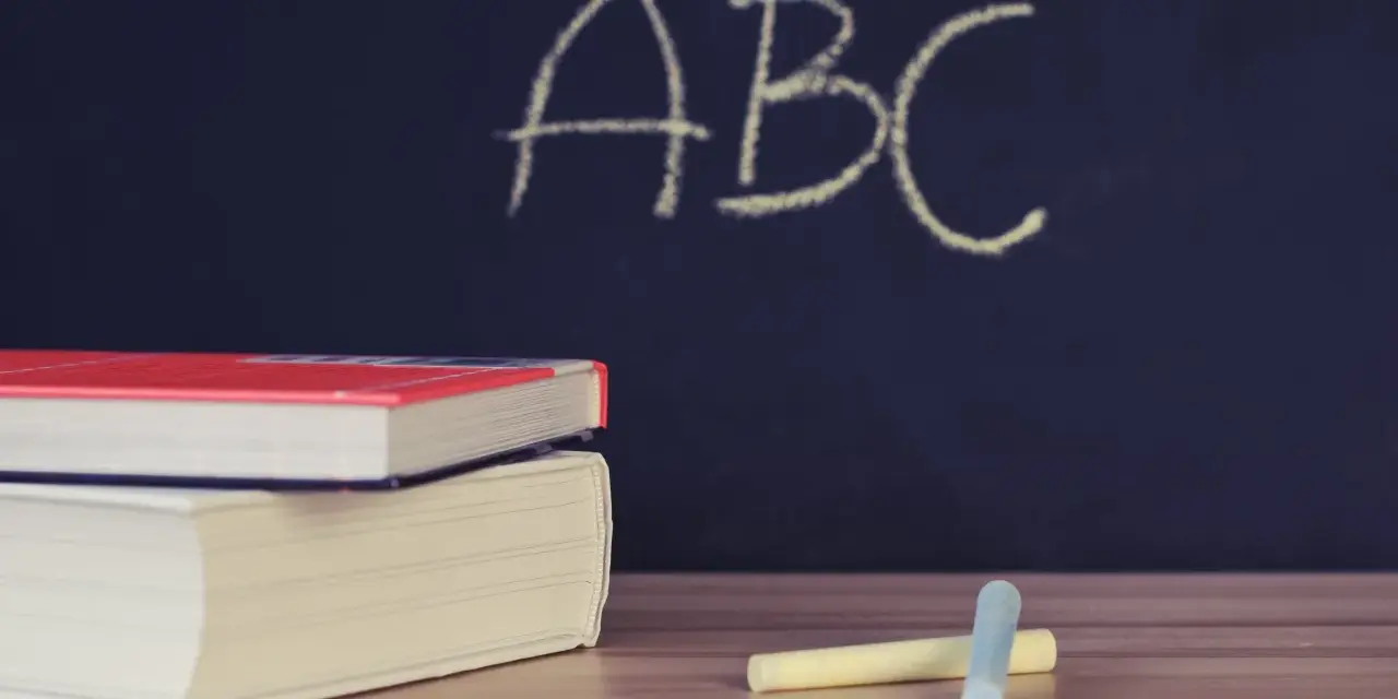 Libri e gessetti su un tavolo di legno, con la scritta "ABC" su una lavagna scura. Un'immagine che evoca l'inizio di nuovi percorsi di apprendimento, come i **corsi abilitanti**.