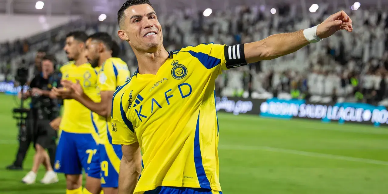 Uśmiechnięty Cristiano Ronaldo w żółtej koszulce Al Nassr, świętujący sukces. Jego zarobki w Arabii Saudyjskiej budzą podziw.