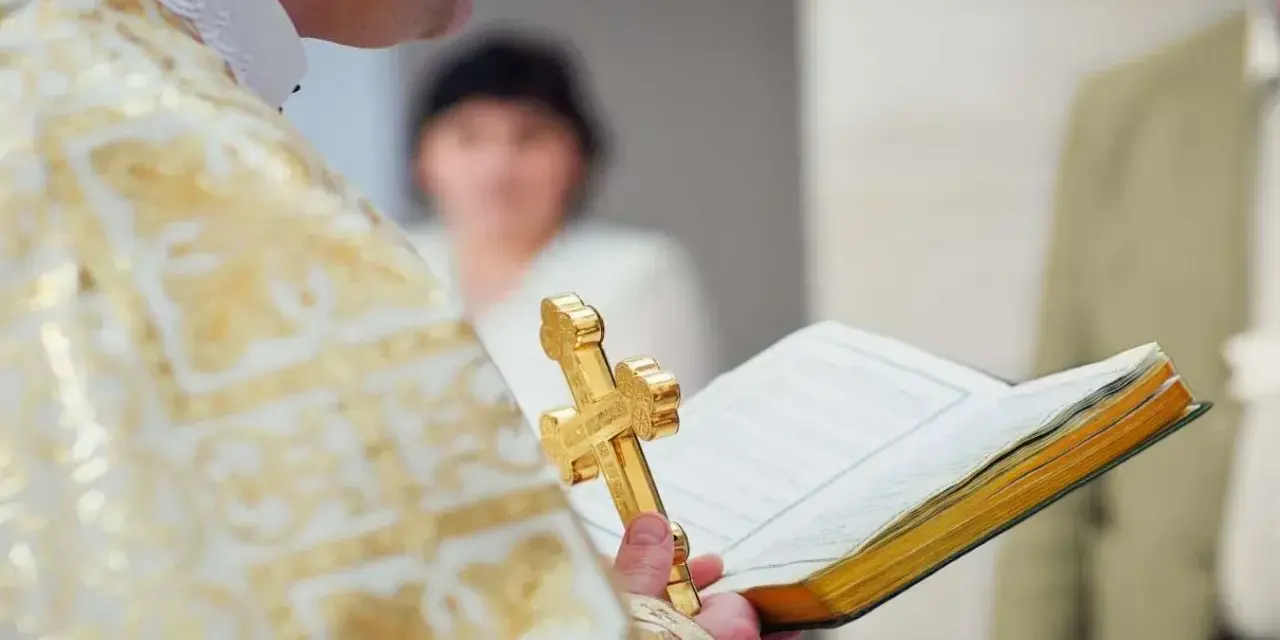 Ksiądz w złotej szacie trzyma krzyż i księgę podczas uroczystości. To ważny moment, kiedy odbywa się bierzmowanie.