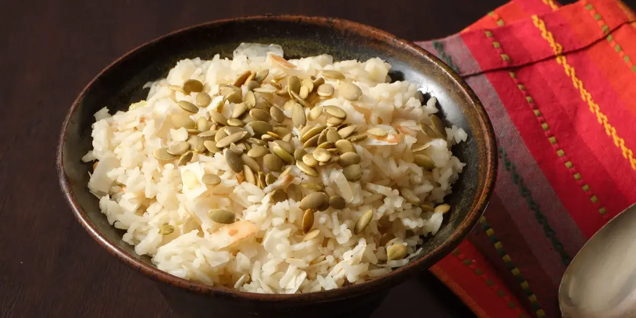 Un tazón de arroz de coco con semillas de calabaza y coco rallado, servido sobre una servilleta colorida.