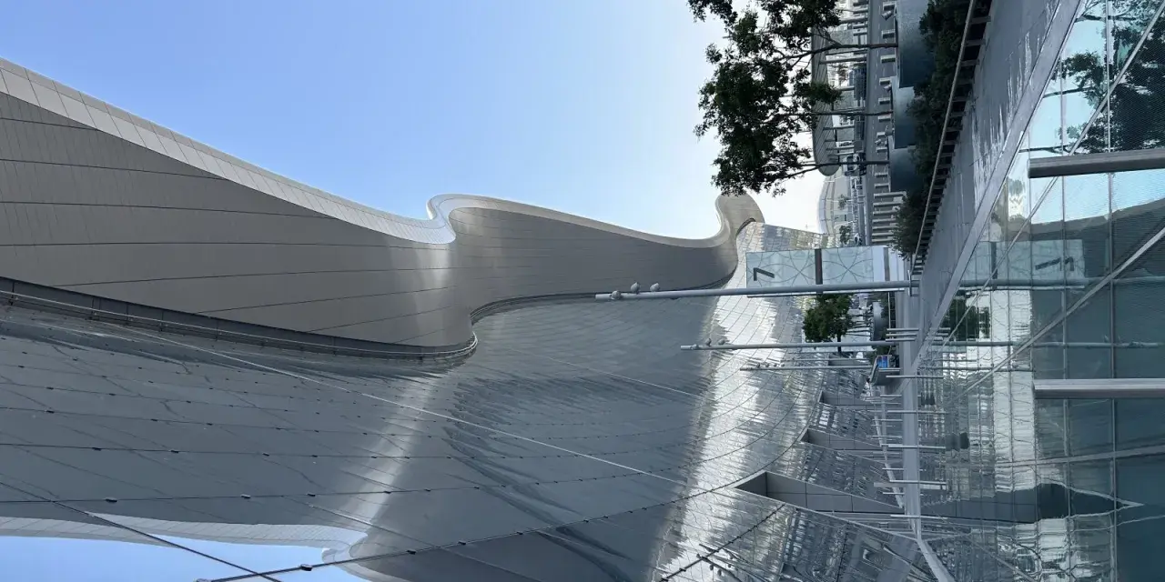 Nowoczesna architektura AUH Zayed International z falującym dachem i szklanymi fasadami odbijającymi niebo i zieleń.
