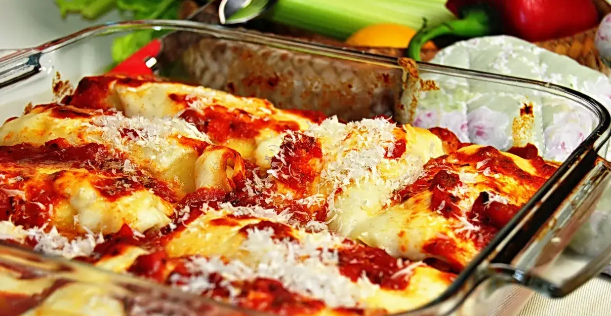 Pyszne, zapiekane cannelloni w sosie pomidorowym, posypane parmezanem. Obok świeże warzywa, idealne do dania.
