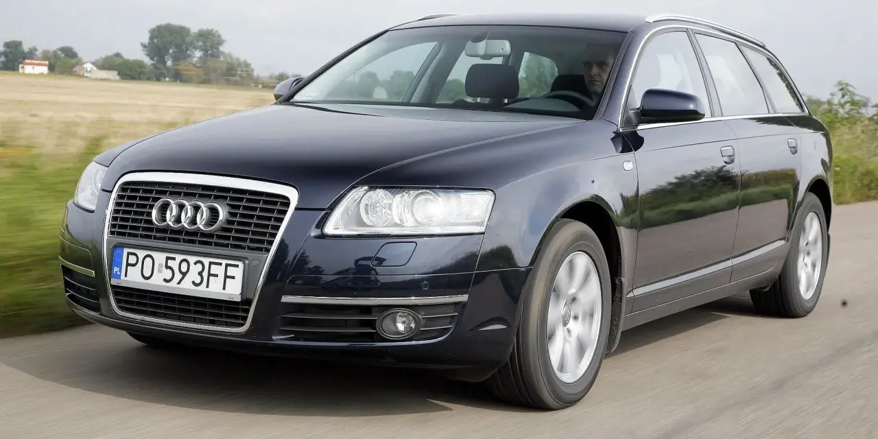 Ciemnogranatowe Audi A6 C6 3.2 FSI Avant w ruchu. Kierowca za kierownicą. Wady tego modelu mogą dotyczyć np. układu napędowego.