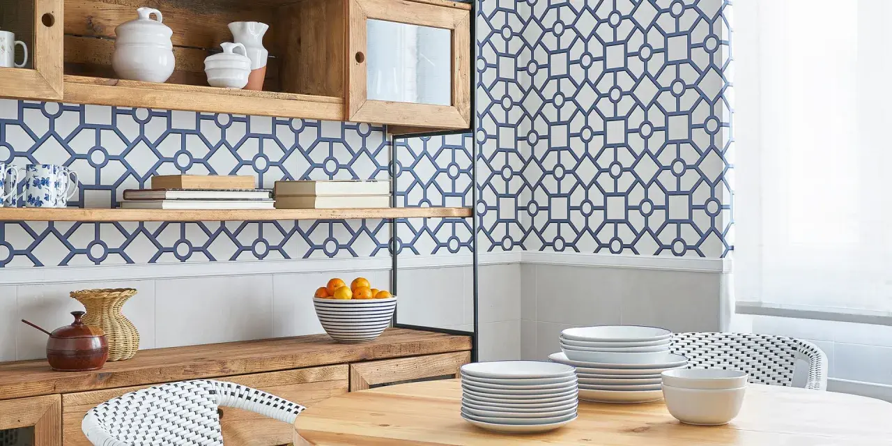 Cocinas con papel pintado azul y blanco, estanterías de madera, vajilla y una mesa de comedor.
