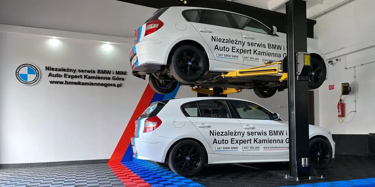 Dwa białe BMW, jedno na podnośniku, w serwisie Auto Expert. W tle logo BMW.