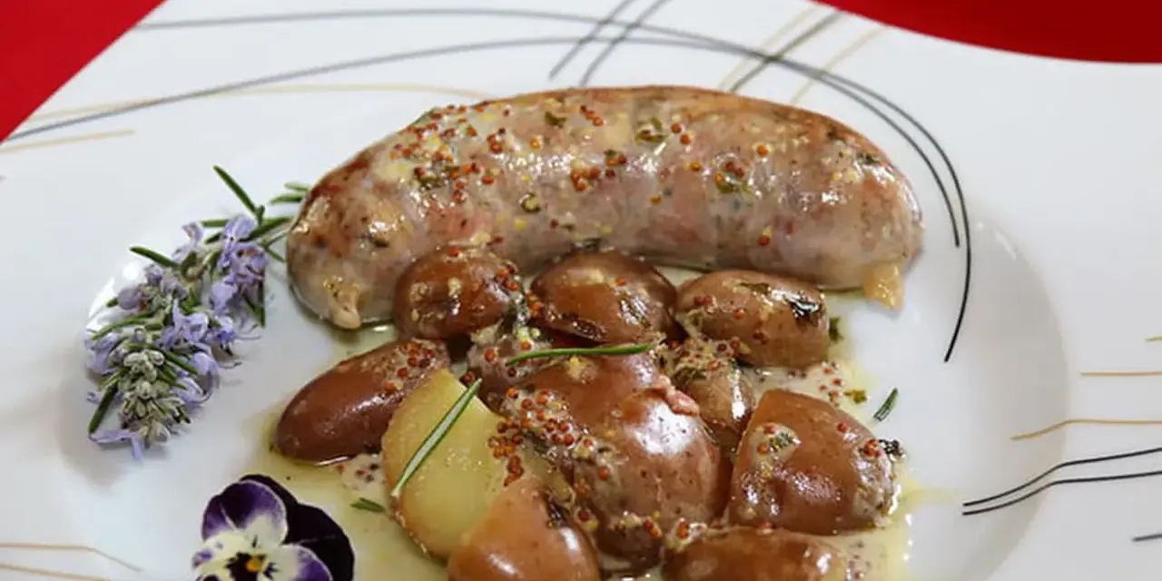 Une andouillette sauce moutarde, accompagnée de pommes de terre grenaille et garnie de romarin et d'une pensée.